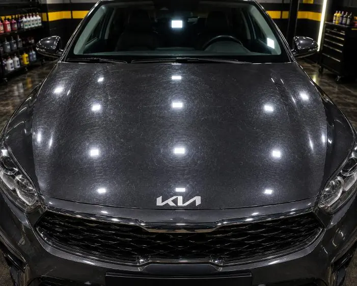Swirl marks showing on a dark bonnet under studio lights before correction